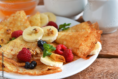 Homemade pancakes with banana, berries and honey for breakfast.