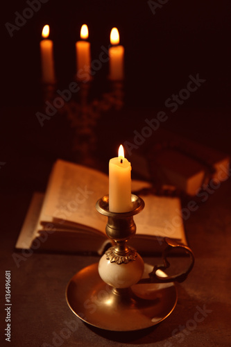 Burning candle with  Bible on background
