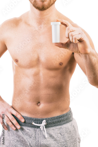 Muscular young man holding a bottle of pills isolated on white background