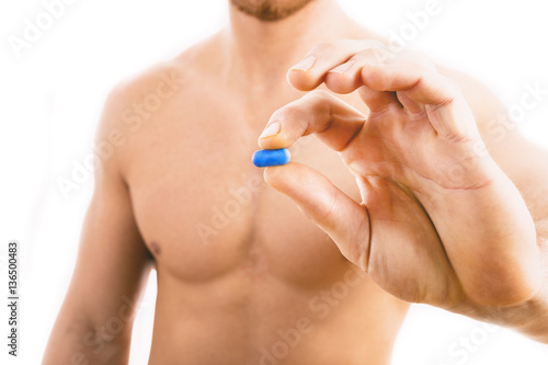 Muscular young man holding blue pill isolated on white background