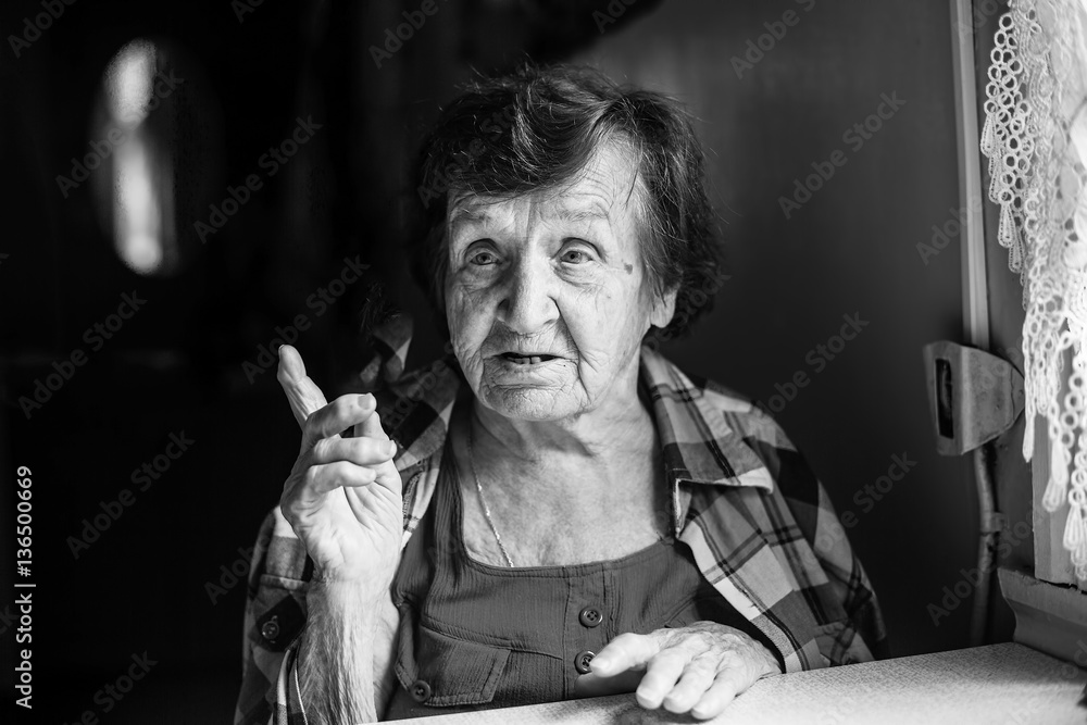 Elderly woman talking sitting at the table. Black-and-white photo.