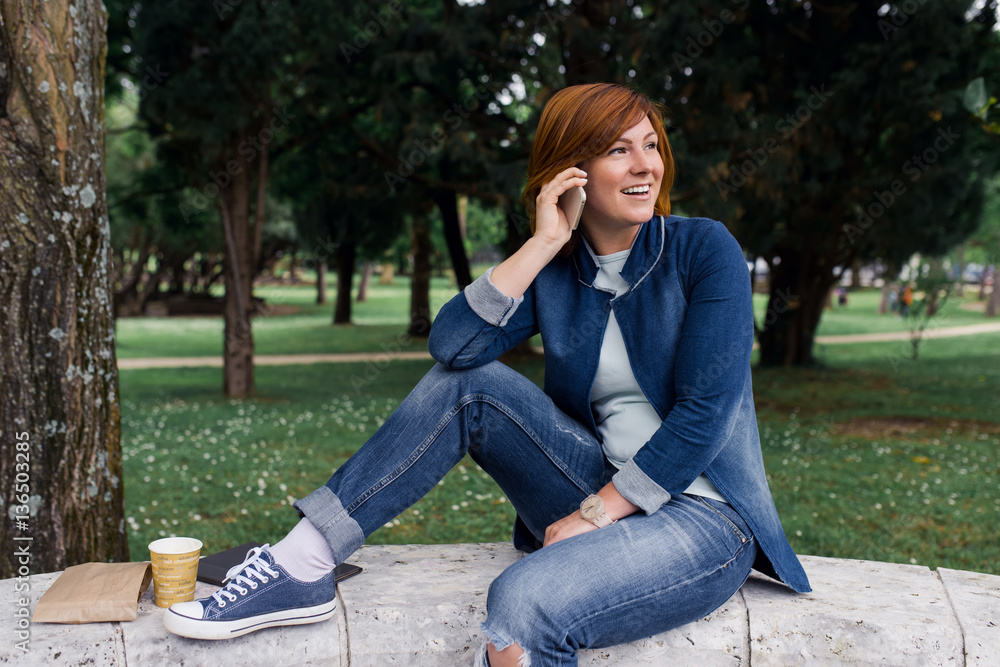Beautiful woman talking on the phone while sitting in the park Beautiful woman talking on the phone while sitting in the park