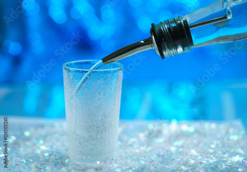 Russian vodka from the bottle is poured into a glass on a blue