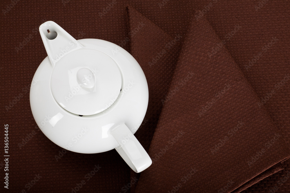 top view of a white teapot and tea strainer on a brown  tablecloth