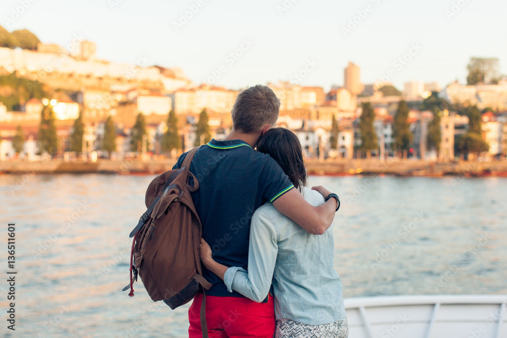 Young couple hugging on the banks of the river and looks out on the town
