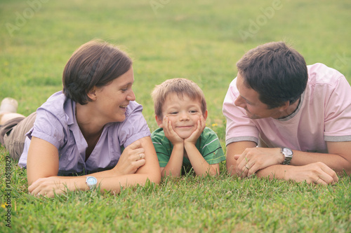 happy blond caucasian kid outdoor family portrait at park with his mum and dad