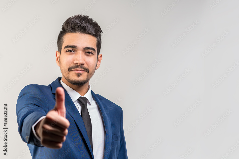 Young attractive man in a blue suit showing thumb up on a gray background. Isolated Young attractive man in a blue suit showing thumb up on a gray background. Isolated