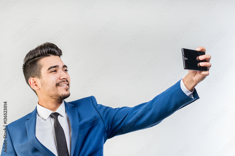 Young attractive man in a blue suit looking at the phone's screen on a gray background. Isolated Young attractive man in a blue suit looking at the phone's screen on a gray background. Isolated