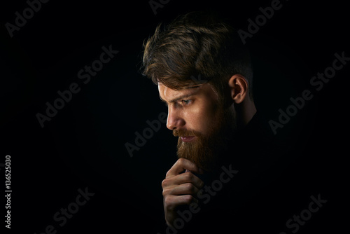 Close-up portrait of puzzled young man touching beard looking do