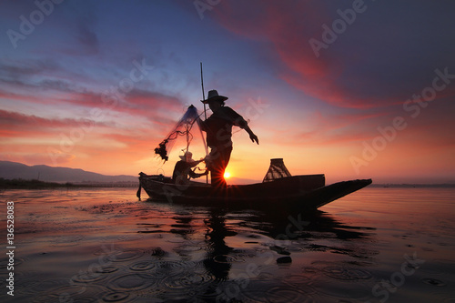 Silhouette of fishermen using nets to catch fish at the Bangpra lake with beautiful scenery of nature during sunrise time. Bang Pra Reservoir at Chonburi province in Thailand
