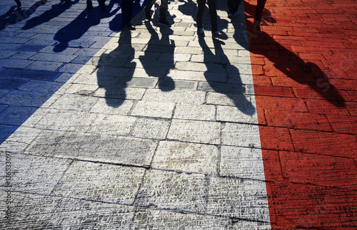 Fototapeta Naklejka Na Ścianę i Meble -  Shadows of group of people walking through the sunny street with painted France flag on the floor.