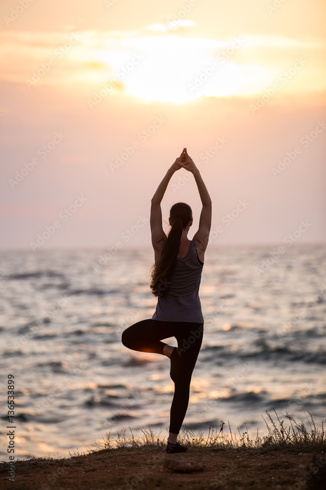 Silhouette of a girl that does yoga at sunset near the sea
