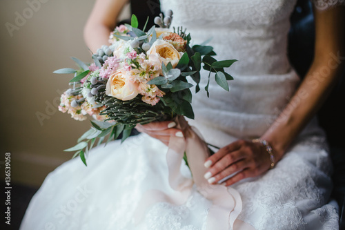 bride in dress sitting on chair and holding wedding bouquet of f