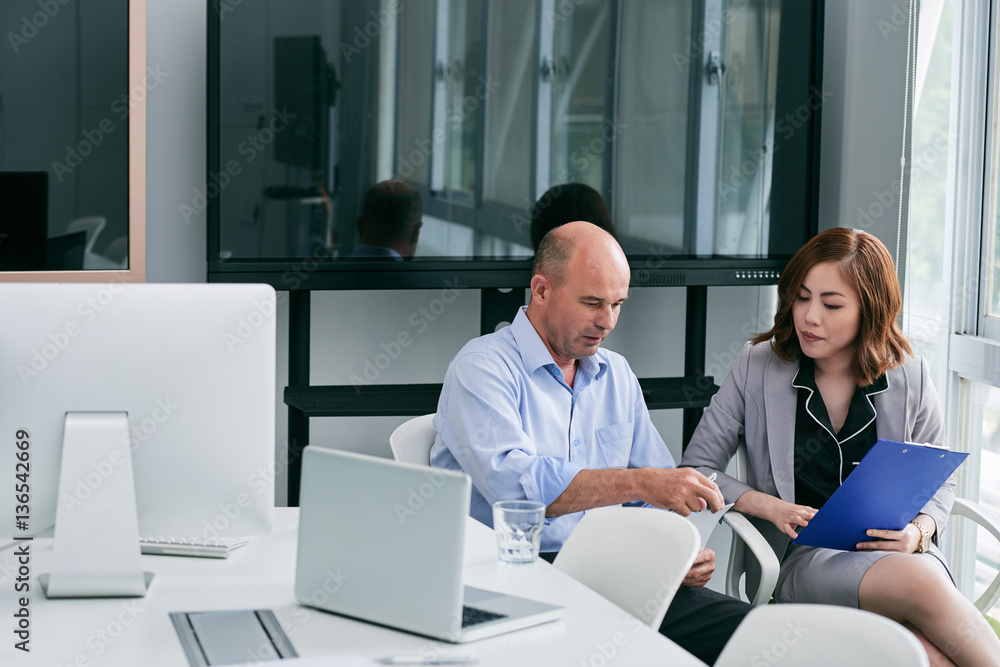 Middle-aged manager and his pretty young colleague sitting in office and working on business presentation Middle-aged manager and his pretty young colleague sitting in office and working on business presentation