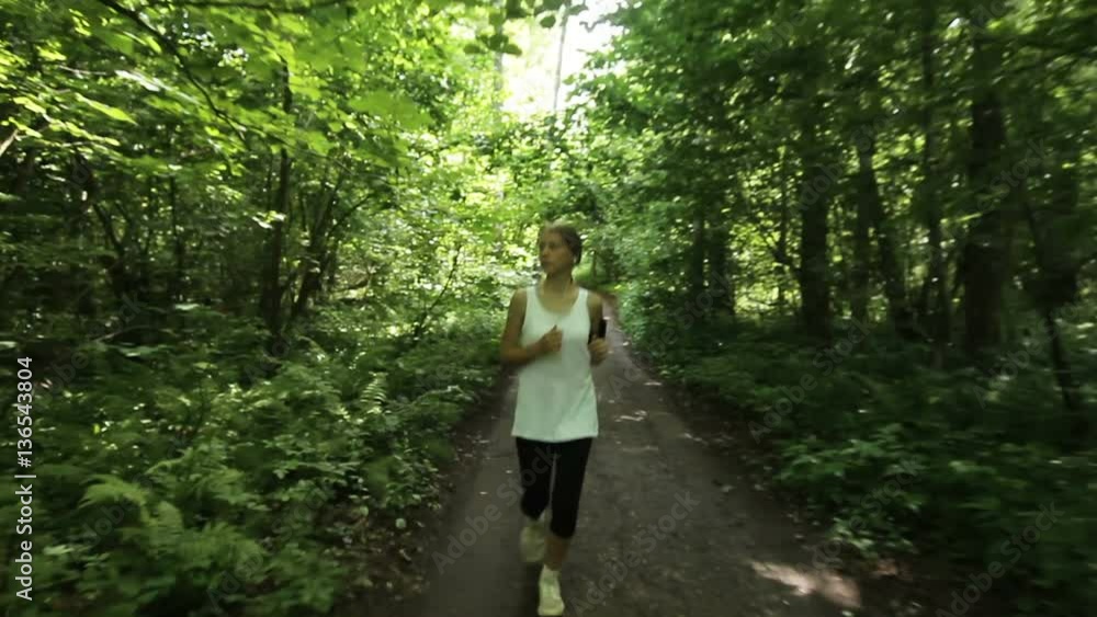 Beautiful teenage girl running in green park on sunny summer day.Young beautiful girl running and listening to music with headphones. Beautiful teenage girl running in green park on sunny summer day.Young beautiful girl running and listening to music with headphones.