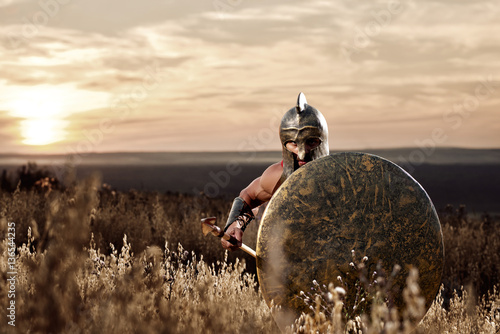 Fotografie Soldier like spartan in bronze helmet holding  rounded shield.