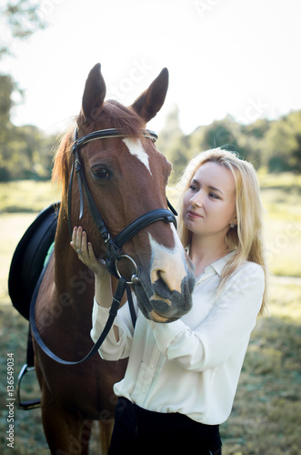 Девушка со светлыми волосами гладит коричневую лошадь 