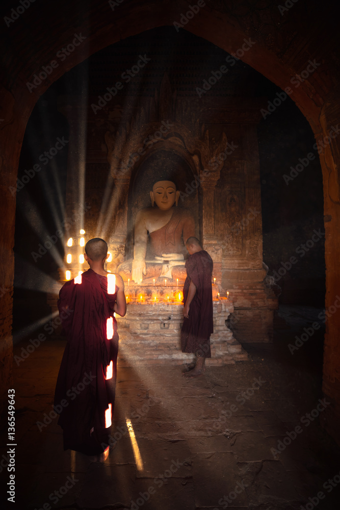 Novices praying with candles in front of buddha statue inside old pagoda, Bagan Myanmar