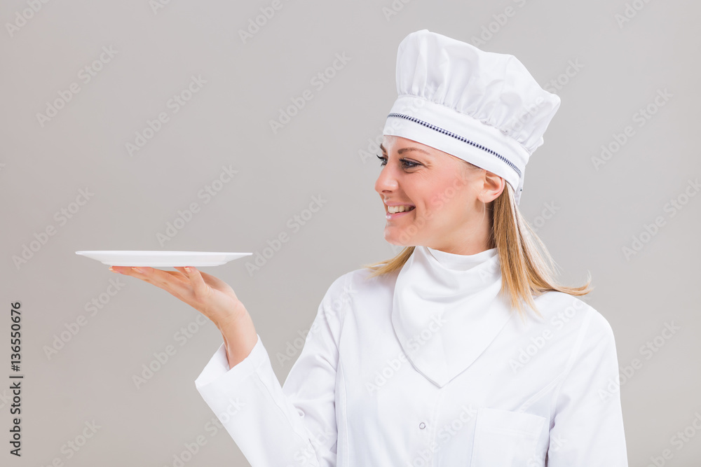 Beautiful female chef is holding plate on gray background. Beautiful female chef is holding plate on gray background.