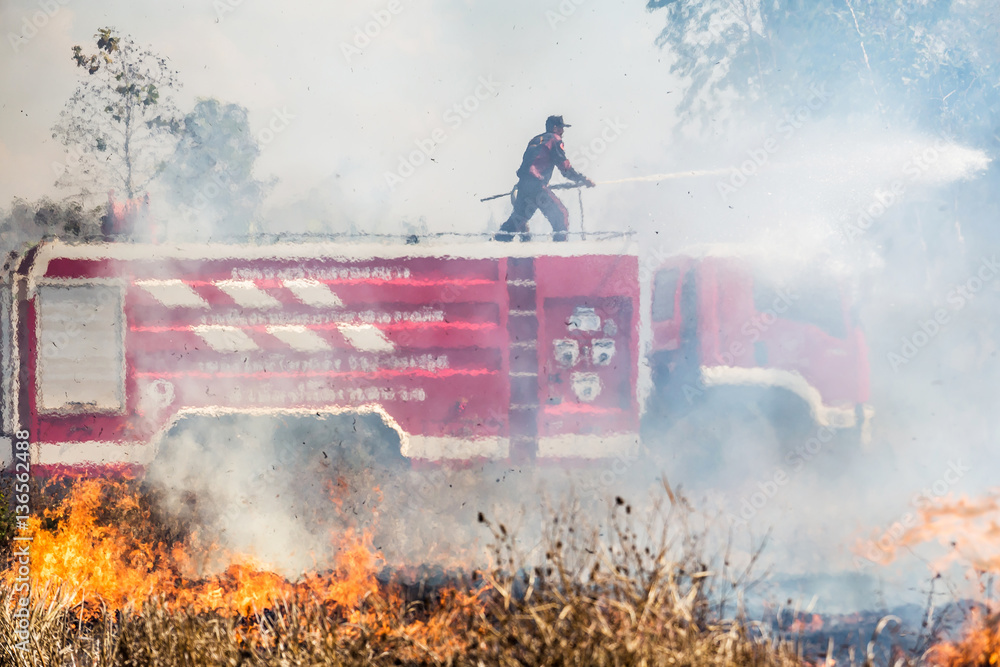 Obraz premium The fireman on fire truk with hose extinguish a fire