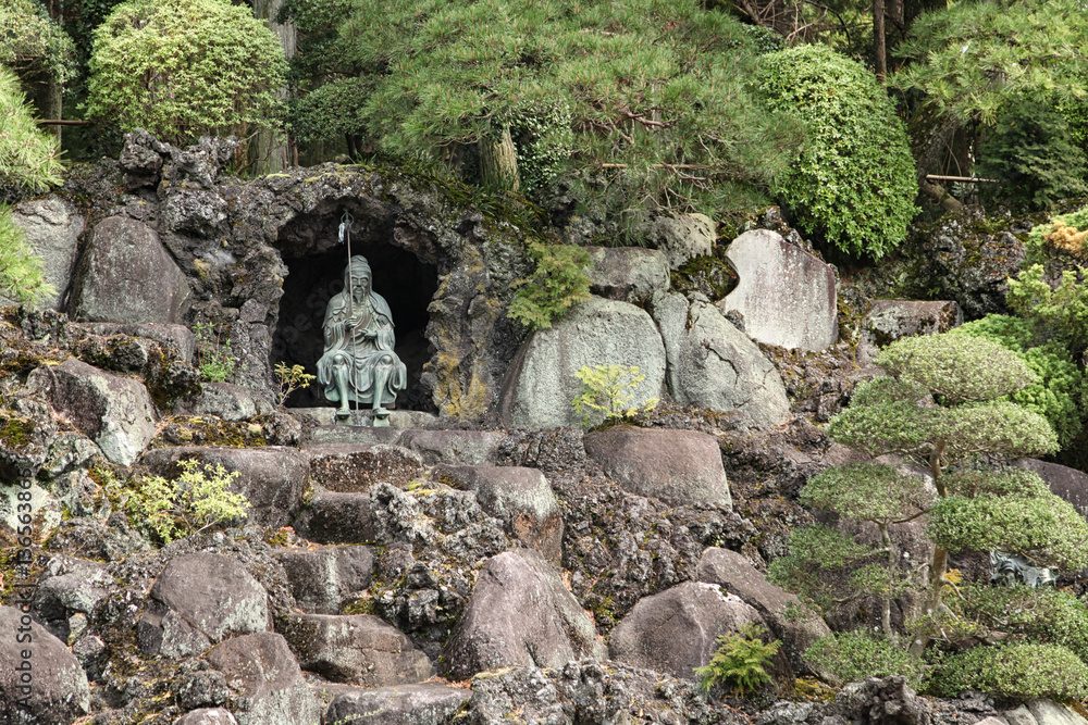 bonsai trees growing outdoor in a garden on a slope with a statu