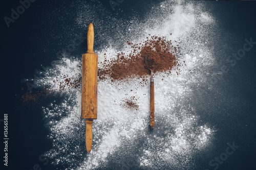 wooden rolling pin with flour and a spoon of cocoa on a black and blue background. Concept: creative chaos.
