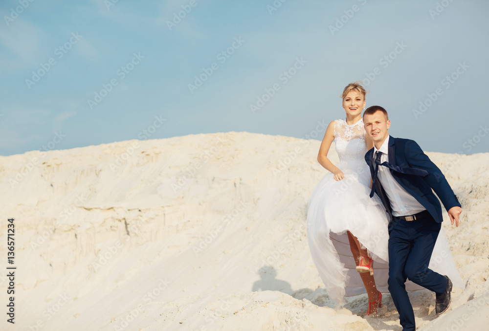 Joyful newlyweds are running on the white sand