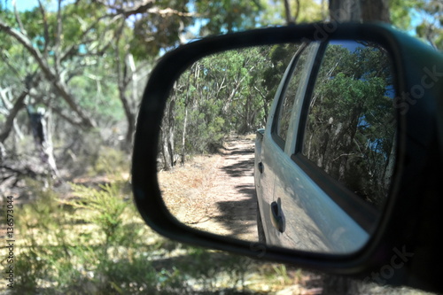 Reflections in a side view mirror of a car driving in the bush. Rear view car mirror in forest live green. Dirt road leading up to a slavery plantation. Concept of 4wd off-road driving in the nature.