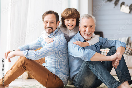 Cute delighted child hugging his father and grandfather