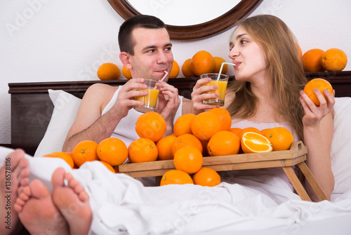 man and girlfriend drinking squeezed orange juice in bed photo