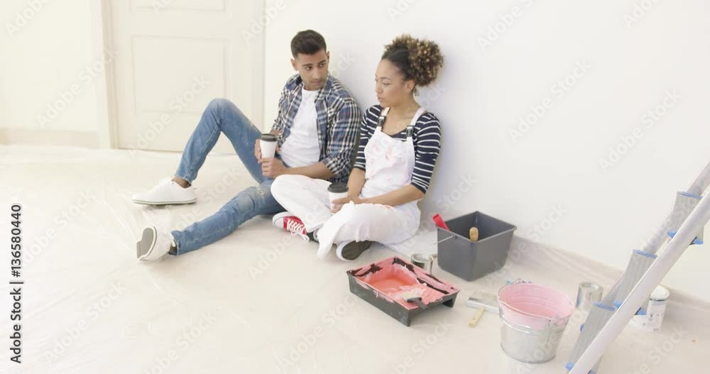 Young couple taking a break from painting their apartment sit on the floor with cups of takeaway coffee having a serious discussion Young couple taking a break from painting their apartment sit on the floor with cups of takeaway coffee having a serious discussion
