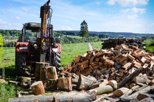 Tractor with log splitter next to pile of firewood