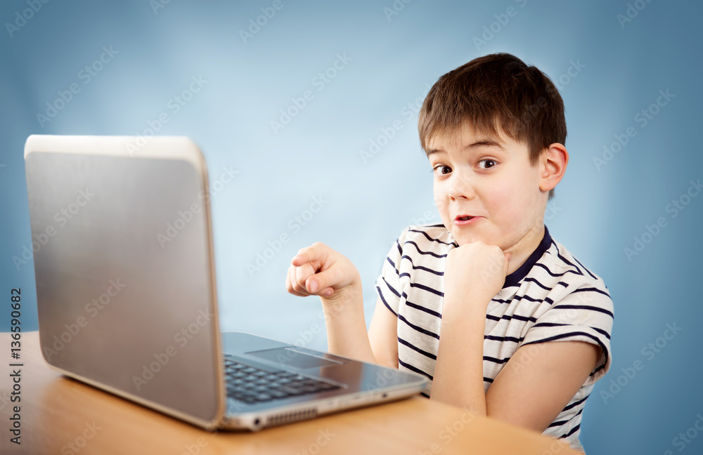 surprised seven years old child sitting with a laptop at table surprised seven years old child sitting with a laptop at table