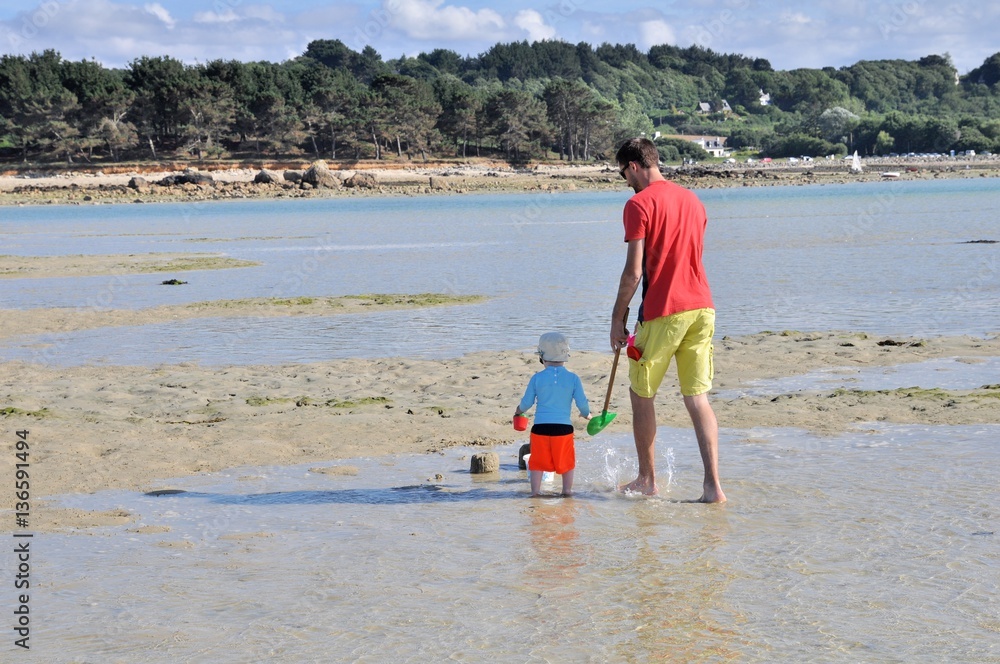 Un père et son fils marchent dans l'eau sur une plage à marée en Bretagne Un père et son fils marchent dans l'eau sur une plage à marée en Bretagne