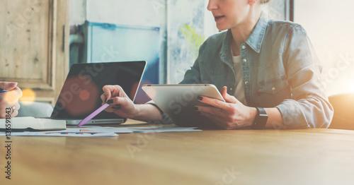 Teamwork. Businesswoman sitting at table and holds tablet computer while showing pen on charts on table. On contrary woman sitting and making notes in notepad. Students learning online, freelance.