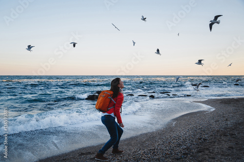 Young happy girl with orange backpack feeding seagulls sea