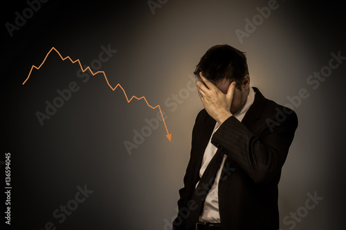 Business man holding hand on his face with falling graph