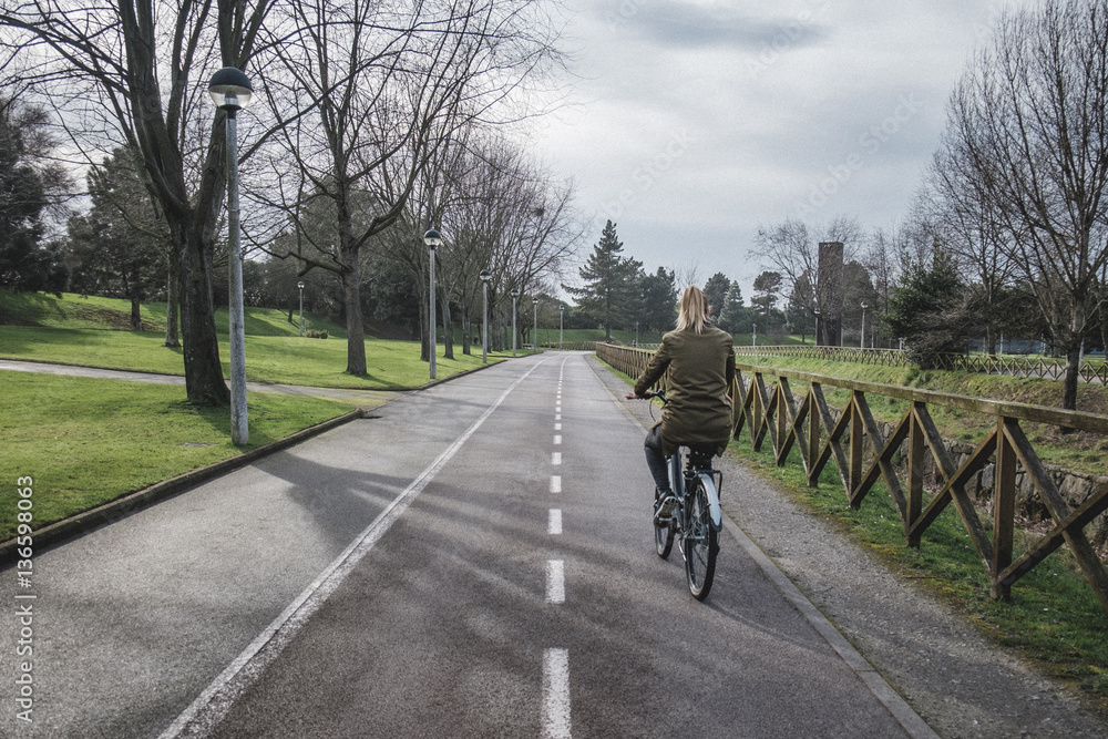 A beautiful blonde woman riding a bicycle along a bike path in a city park A beautiful blonde woman riding a bicycle along a bike path in a city park