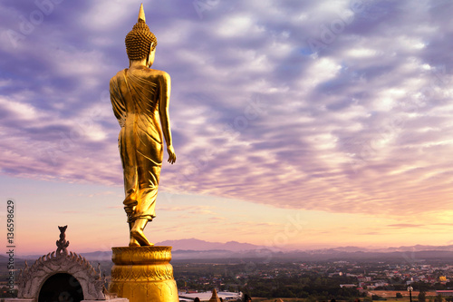 Golden Buddha standing at Wat Phra That Kho Noi with colorful sky, Nan Province, Thailand