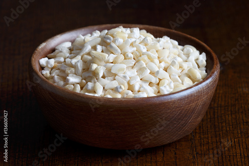 Dehulled dried corn in brown wooden bowl isolated on dark wood. photo