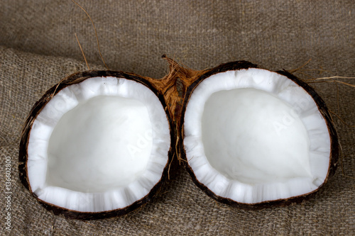 Two halves of a coconut with a peel on a background of a sacking