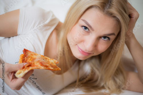 Beautiful girl eating pizza  Cheerful blond woman sitting on a bed  Very beautiful Russian girl  Sport woman eating junk food