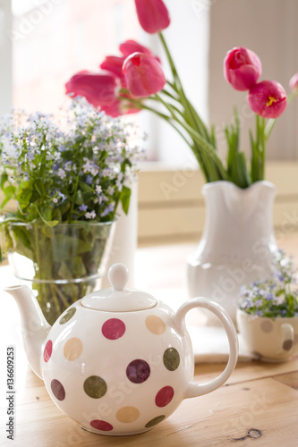 Teapot with dots and vases with beautiful spring flowers on the wooden table. Decoration for home interior. Forget-me-not and tulips in vases. Flowers from the garden.Tea time and table setting.