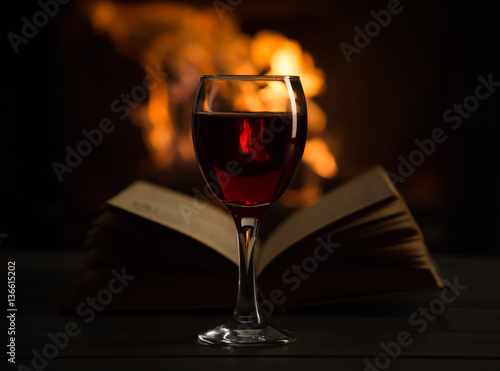Open book with red wine in front of the fireplace.