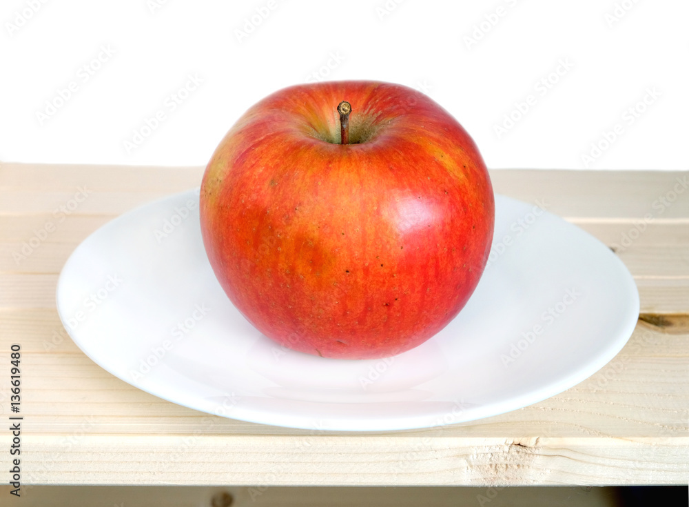 Big ripe red apple on white plate in wooden shelf on white background front view closeup Big ripe red apple on white plate in wooden shelf on white background front view closeup