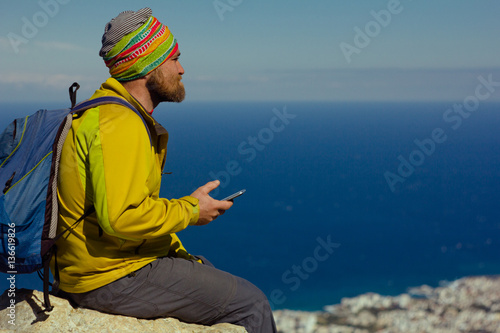 man sits on a cliff above the sea with a smartphone in hand