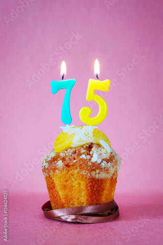 Muffin with burning birthday candles as number seventy five on pink background