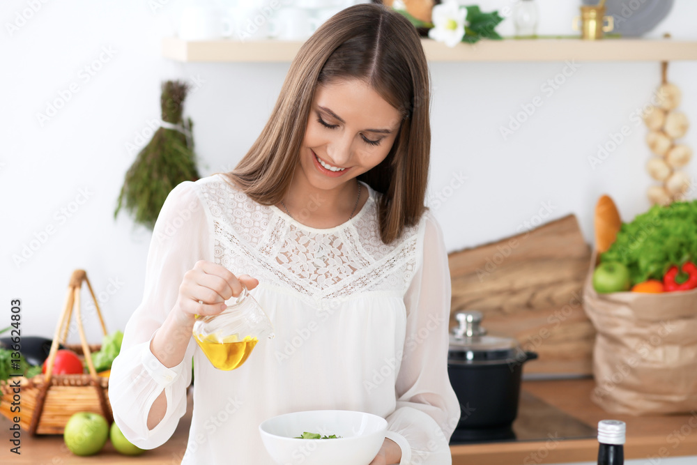 Young happy woman is cooking or eating fresh salad in the kitchen. Food and health concept