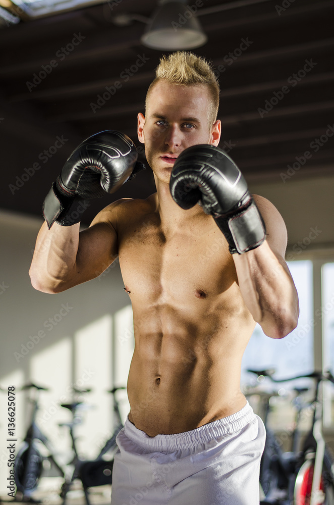 Attractive shirtless young man with boxing gloves, looking at camera