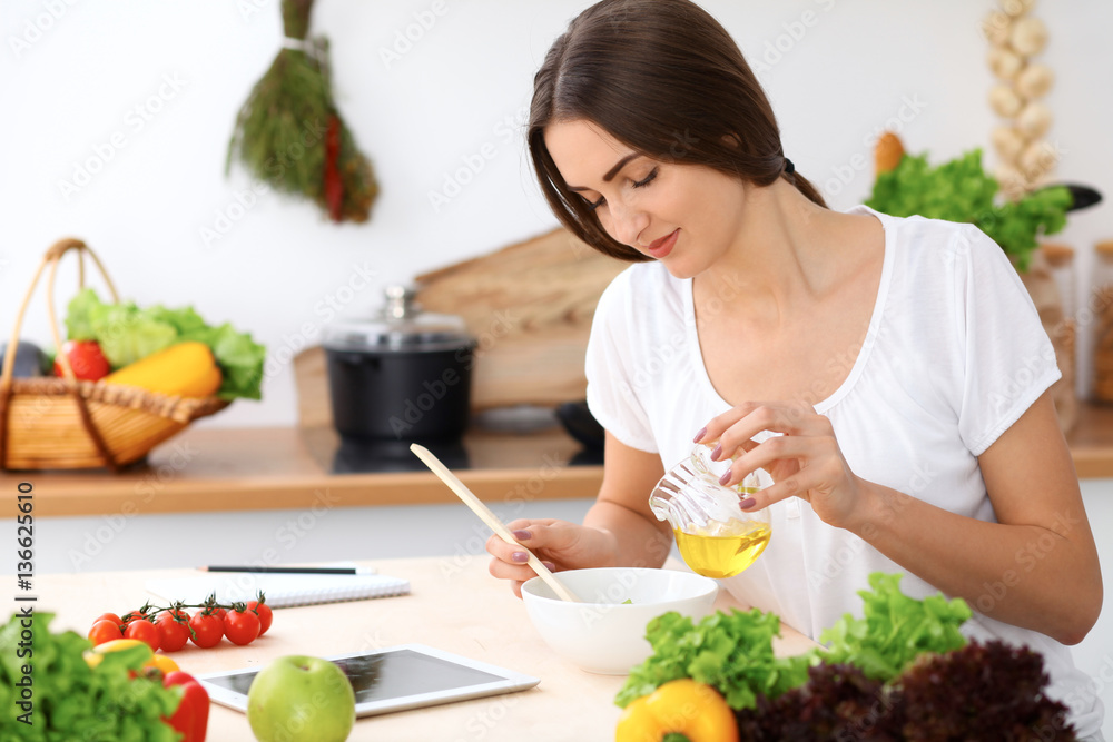 Beautiful Hispanic woman is cooking in the kitchen. Housewife is tasting fresh salad while sitting at the table Beautiful Hispanic woman is cooking in the kitchen. Housewife is tasting fresh salad while sitting at the table